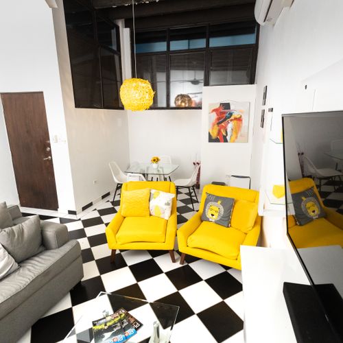 Experience vibrant comfort in this inviting living room. With a large grey sofa, cheerful yellow cushions, and two additional seats, there's ample space for everyone to gather. Enjoy entertainment on the smart TV in this lively and welcoming space.