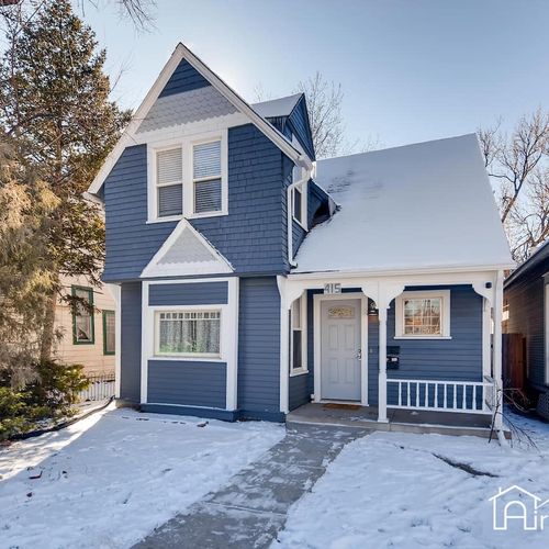 Charming two story blue home with crisp white trim, a snow covered yard, and a welcoming covered entry.