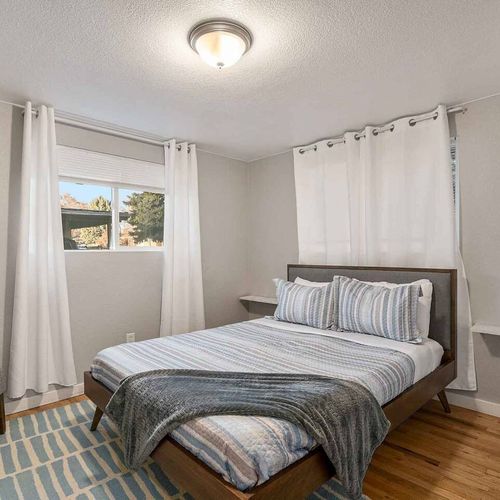 - queen bedroom with soft wood floors, striped linens, and large windows for natural light
- clean design with modern bed frame, white blackout curtains, and subtle coastal vibes
- calming and restful space perfect for solo guests or couples