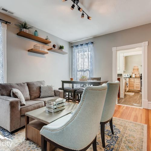 - spacious living area with plush seating & mounted tv flows effortlessly into the dining space
- floating shelves, patterned curtains, and hardwood floors add charm throughout
- seating for four at the dining table makes mealtime easy and enjoyable