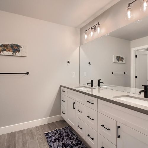 - modern bathroom with a wide dual sink vanity and sleek matte black fixtures
- wood look flooring and accent rug bring warmth to the minimalist space
- large mirror and clean design offer both style and convenience for guests