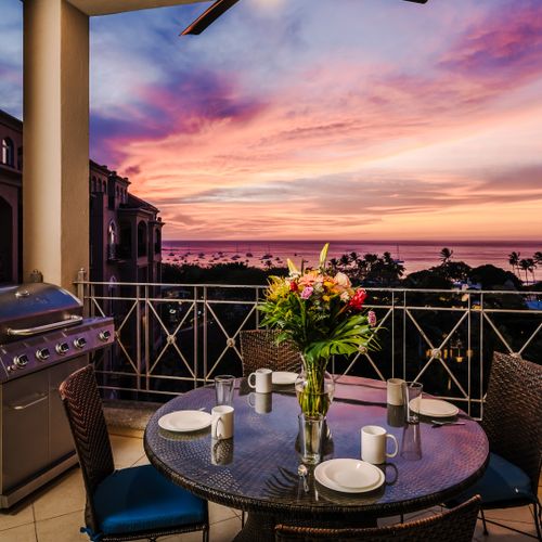 Balcony at sunset overlooking the lit resort pool, palm tops, and Tamarindo Bay under a pink-purple sky.