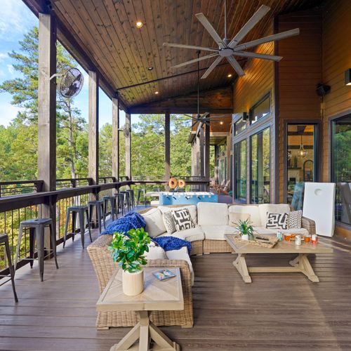 The covered lounge area provides plush, all-season comfort, while the lookout bar running along the deck railing invites guests to sip, snack, and soak in breathtaking panoramic views of the surrounding woods.