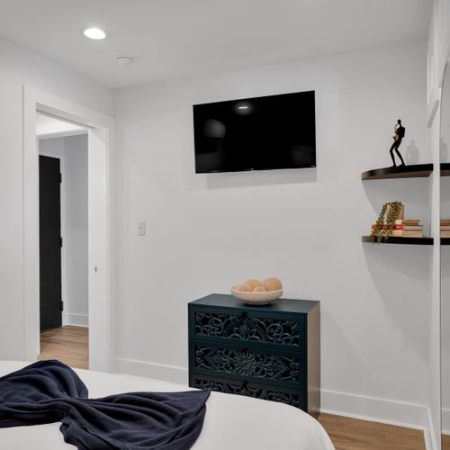 Bedroom 1 w/ a wall-mounted TV & minimalist shelf for a clean, clutter-free feel.