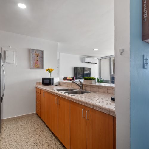 Kitchen space featuring light brown tiled counters, stainless steel double sink, and ample wood cabinets for storage.