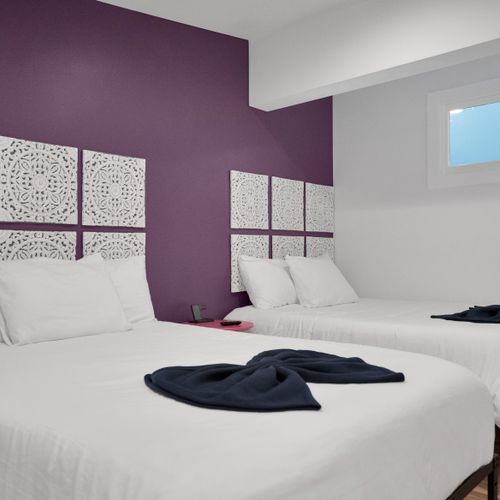 Bedroom 2 w/ plush white bedding & a dramatic purple accent wall for moody rest.