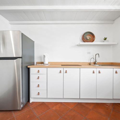 This efficient kitchenette features modern white cabinetry with sleek hardware, a practical countertop, and a full-sized stainless steel refrigerator. Perfect for convenient meal prep.