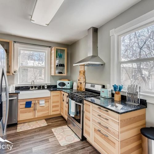 - fully equipped kitchen with stainless steel appliances, farmhouse sink, and range hood
- light wood cabinetry and black granite countertops provide a sleek modern vibe
- dual windows and stylish blue accessories brighten up the entire space