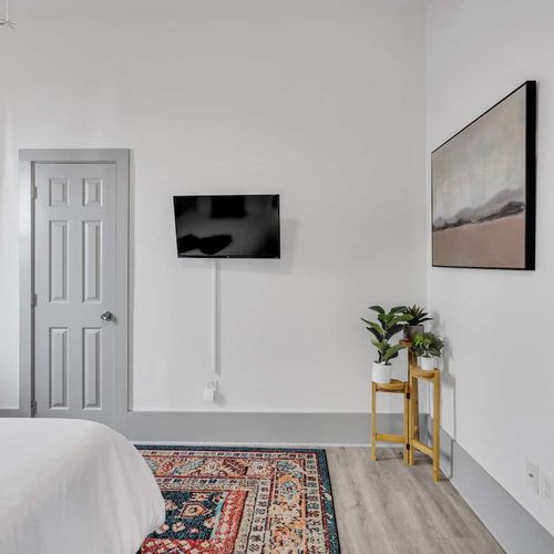 Bright bedroom w/ mounted TV, cozy bed, & soft lighting for a relaxing wind-down.