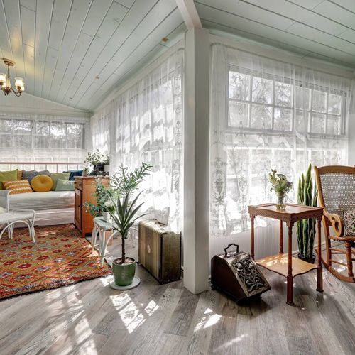Sun-drenched enclosed porch with plush seating and forest views all around.