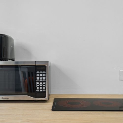 A modern kitchen countertop with a microwave oven, a coffee maker, and an induction cooktop against a plain wall.