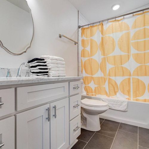 Cheerful bathroom w/ a bold patterned curtain & classic round mirror.