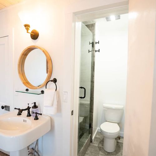- fresh and functional ensuite with pedestal sink, round wood framed mirror, and sconce lighting
- glass door shower with sleek tile and modern black fixtures
- clean and simple layout perfect for refreshing after a day of adventure