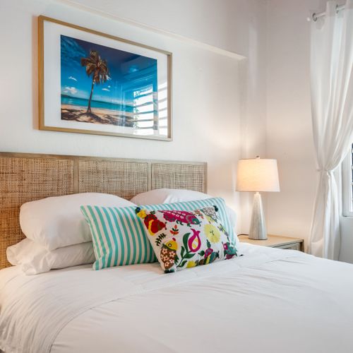 Your Personal Oasis: A cozy and bright bedroom awaits, complete with charming bedside lamps and a captivating palm tree print that brings the essence of a beach getaway indoors.
