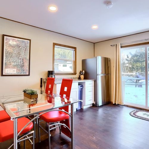 - dine indoors with scenic outdoor views through glass doors that open to nature
- clean modern lines meet rustic vibes with red chairs and wood style flooring
- enjoy meals or morning coffee while soaking in the peaceful snowy backdrop