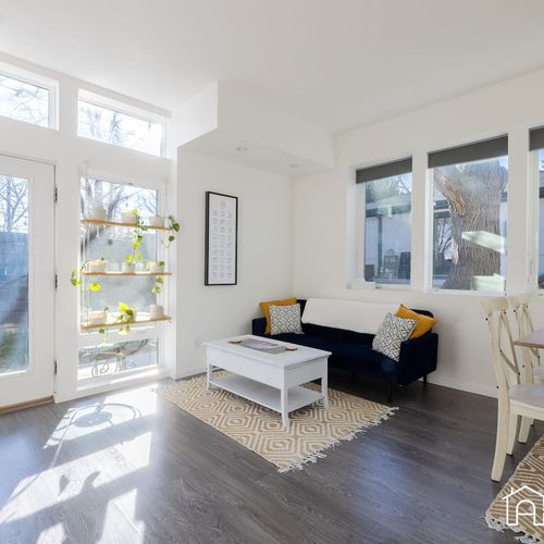 - wake up to sunshine pouring in through large windows and a glass door to the yard
- relax on a plush navy couch with golden accents and enjoy greenery inside and out
- share a meal or work remotely at the charming wood and white dining set