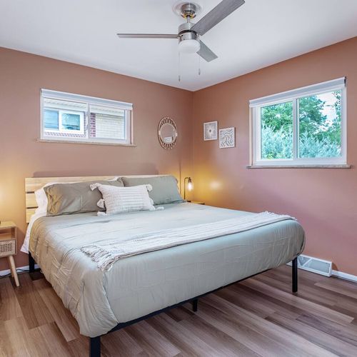 - tranquil bedroom featuring a king size bed with soft linens and earthy tones
- natural light pours in from dual windows, highlighting the cozy modern design
- warm peach walls, wood flooring, and ambient bedside lighting set a relaxing mood