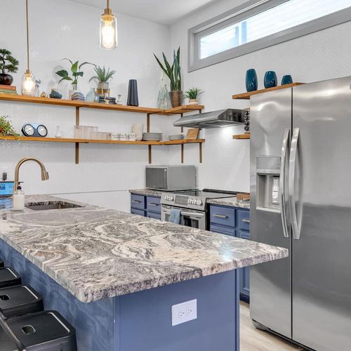 Kitchen w/ marble-look counters, open shelving, & blue cabinetry — sleek & functional.