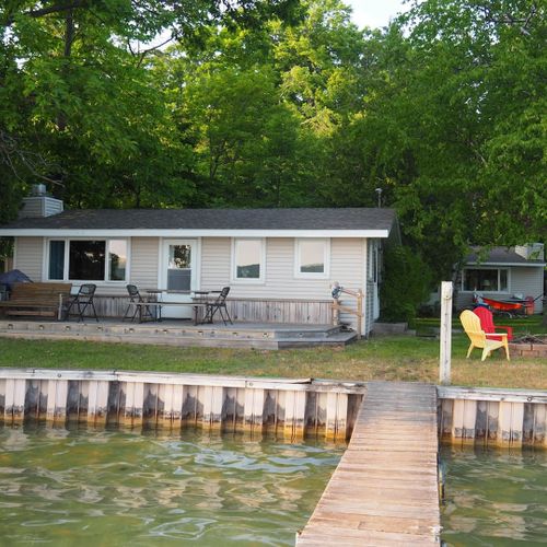 Overall:  the front of the cottage on little glen lake, highlighting the lake, lakefront deck, private dock, and the bonfire ring.