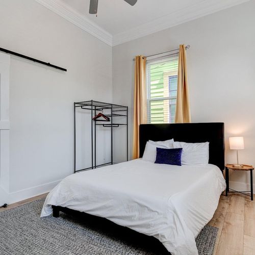 Airy queen bedroom w/ golden curtains & natural light — a calm, restful escape.