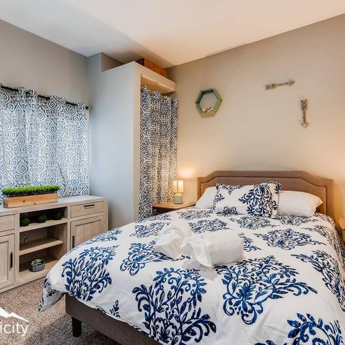 - tranquil bedroom with plush bedding in a blue botanical print and soft bedside lighting
- built in closet nook with matching curtain blends storage with design
- carpeted flooring, wall decor, and natural light complete the relaxing retreat