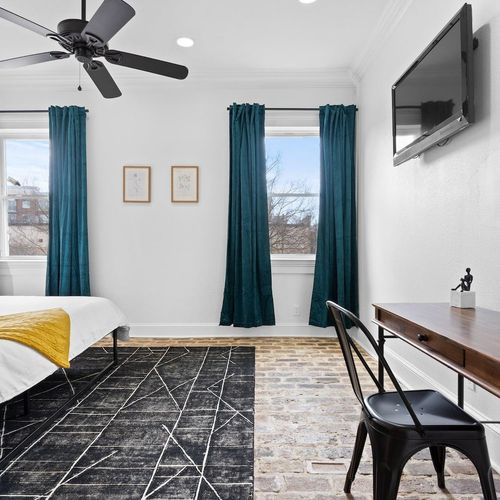 Bedroom 1 w/ charming brick floors & teal curtains for a cozy, character-filled feel.