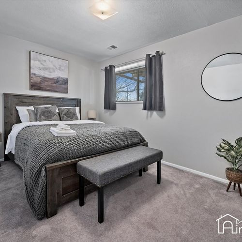 - peaceful bedroom featuring a plush gray comforter, wood bed frame, and cozy bench seat
- blackout curtains and soft carpet create a restful environment for deep sleep
- modern round mirror and potted plant add a touch of chic minimalism