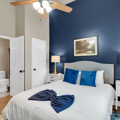 Bedroom w/ navy accent wall, plush pillows & ensuite access for added privacy.