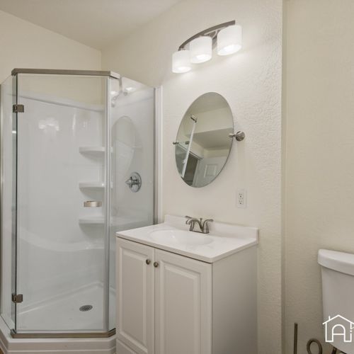 The attached bathroom showcases a glass-enclosed walk-in shower, a vanity with a mounted mirror, and new lighting fixtures.