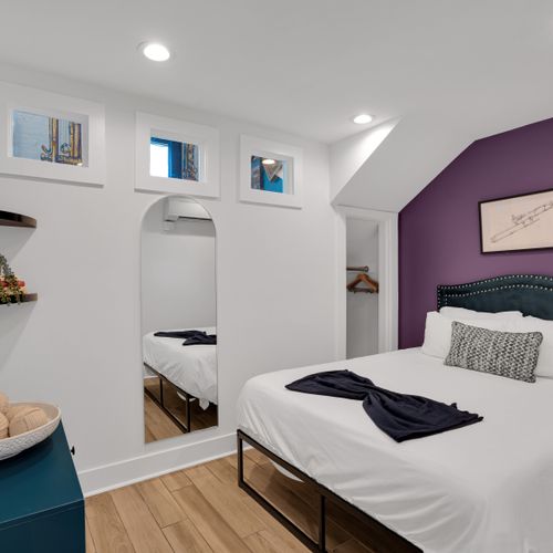 Bedroom 1 w/ crisp white bedding & rich purple accent wall for a moody, restful vibe.