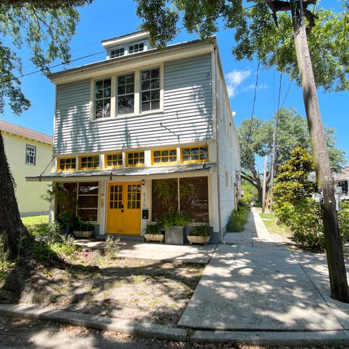 Charming exterior w/ lush greenery & a welcoming yellow front door.