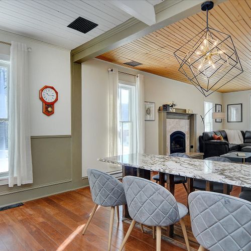 The dining area features a large granite island dining table, plush velvet chairs, and a modern geometric chandelier.