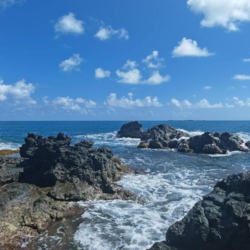 Panoramic oceanfront beauty: azure waters, rolling waves, and verdant cliffs under a captivating sky.