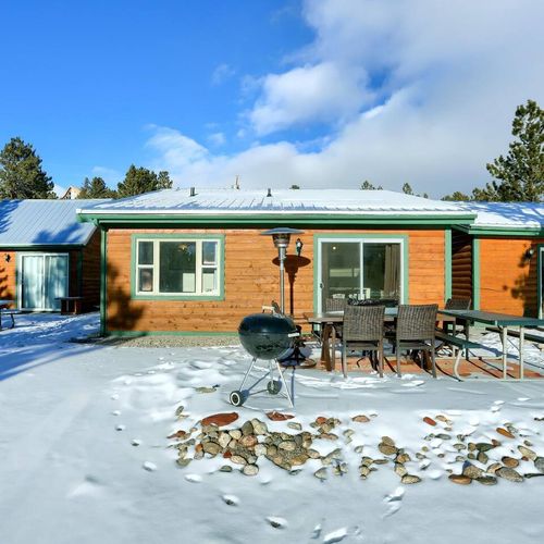 Spacious backyard setup with a grill, dining area, and snowy pine forest ambiance.