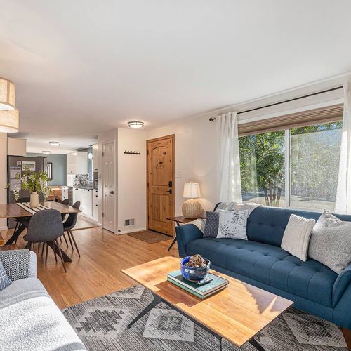 - bright and open living space with a mix of navy and gray seating and large front window
- natural light fills the room, highlighting the cozy textures and decor
- flows seamlessly into dining and kitchen areas for group connection