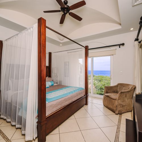 Master bedroom foot-of-bed view showing four-poster king, louvered hardwood closets, TV, and hallway to en-suite.
