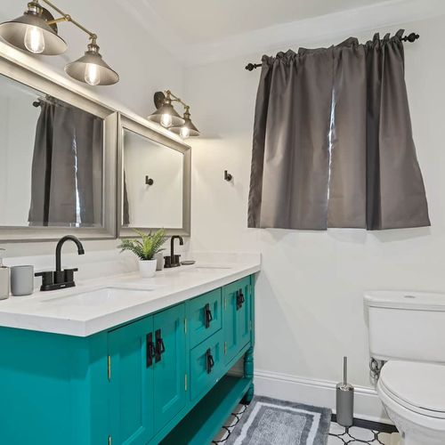 Bright bathroom w/ teal cabinets, a sink & well-lit mirror.
