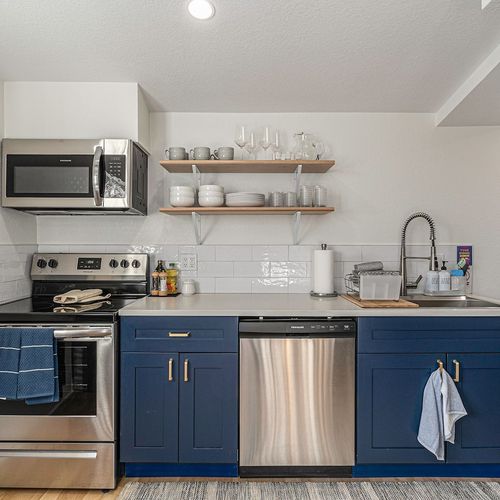 - prepare food with ease using this fully stocked kitchen featuring sleek open shelving
- stainless steel oven, dishwasher, and microwave offer modern cooking convenience
- blue cabinets add bold charm to the space with subway tile backsplash detail
