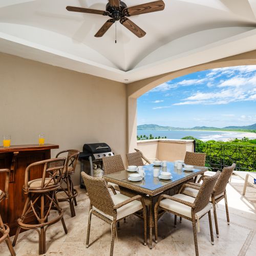 A private balcony with lounge chairs, a dining table, grill, bar, and jacuzzi