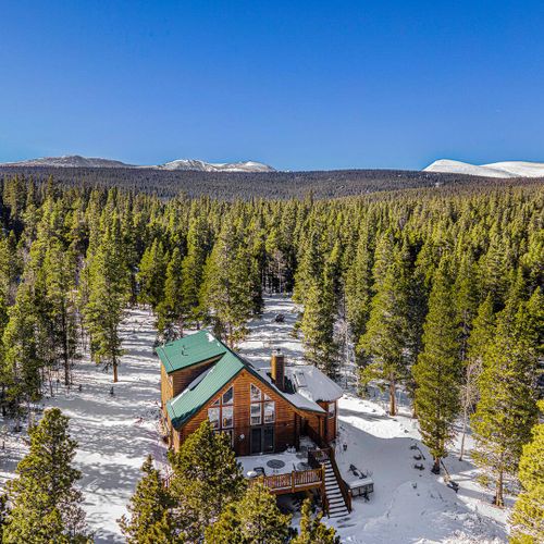 Charming cabin surrounded by snow dusted evergreens and panoramic mountain vistas under clear blue skies.