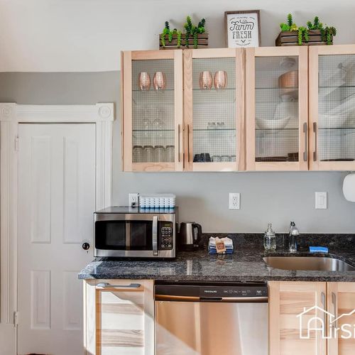 - functional kitchenette includes a microwave, dishwasher, sink, coffee maker, and sleek granite surfaces
- wood and mesh glass cabinets display dishes and copper mugs with style
- pops of green and decorative signs bring a cheerful homey vibe