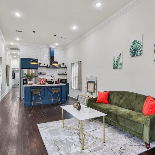 Bright living room w/ a green sofa, white coffee table & a peek into the kitchen.