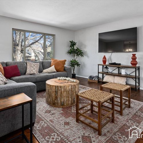 - entertainment ready space with wall mounted tv, console table, & warm wood details
- woven stools & rustic coffee table center the cozy seating arrangement beautifully
- decorated with warm reds and orange tones that feel inviting and comfortable