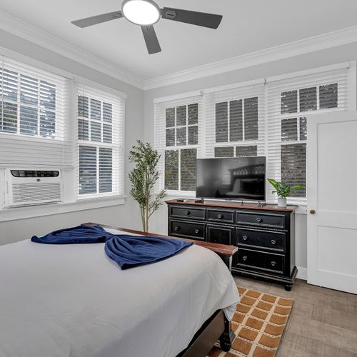 Wake up to sunshine in this bright and airy bedroom, featuring large windows, a cozy bed, and chic decor for a peaceful retreat.