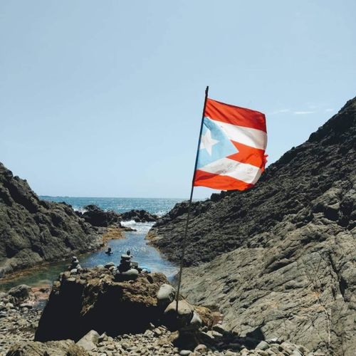 Experience the spirit of Puerto Rico! The vibrant flag proudly flies over a unique rocky cove, leading to refreshing ocean waters.