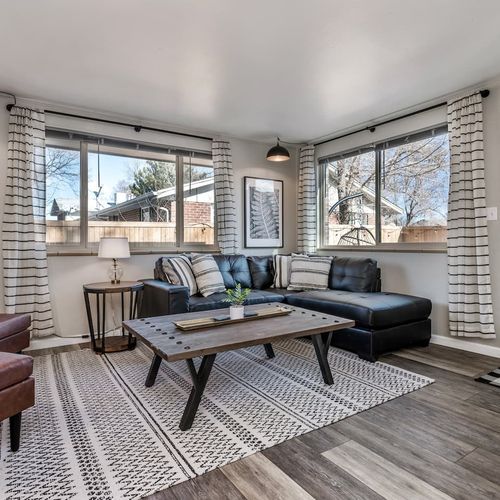 - sun soaked living room with modern black sectional and wide window views
- woodgrain floors and striped rug create a warm stylish base for lounging
- perfect for morning coffee cozy reading time or relaxed evening hangouts