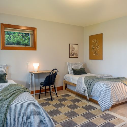 3rd  bedroom with twin trundle beds offers flexible sleeping for families or friends, with a cozy lamp, single couch, and table with chair for relaxing or reading.
