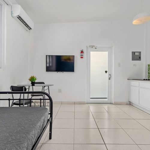 Modern room with cozy sofa bed with soft texture and clean modern kitchennette, airconditioner, window with natural light, white walls, cozy lights