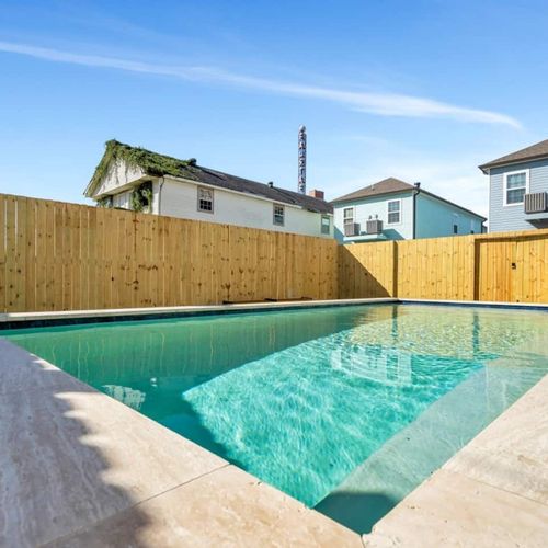 Sparkling pool w/ a gentle water feature tucked behind a tall privacy fence.