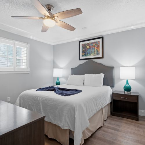 Bright bedroom w/ warm lamp glow & a neatly made bed.